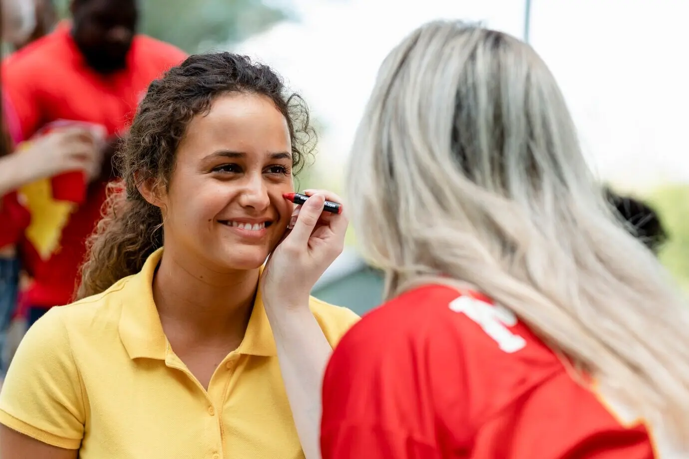 Женщине раскрашивают щёки в цвета её команды.